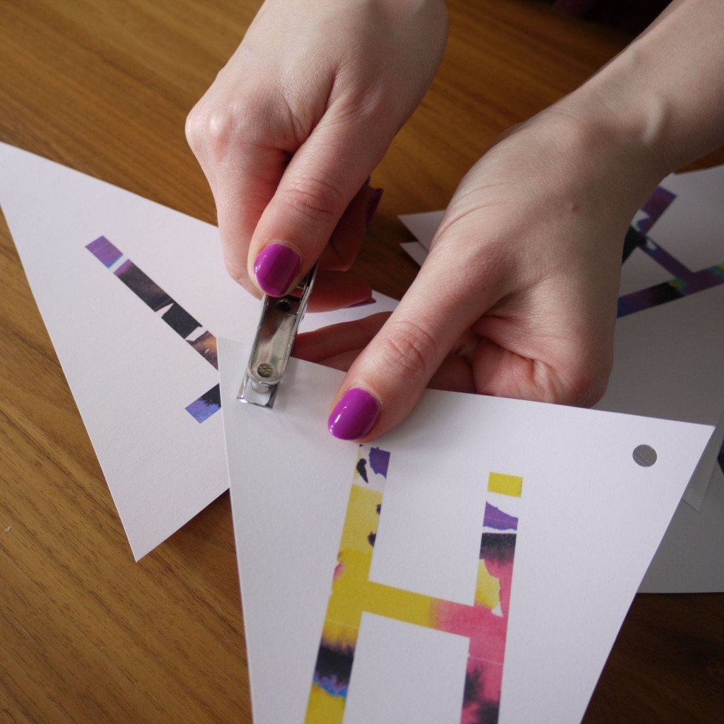 Artisan punching holes in colourful paper craft bunting on a wooden surface