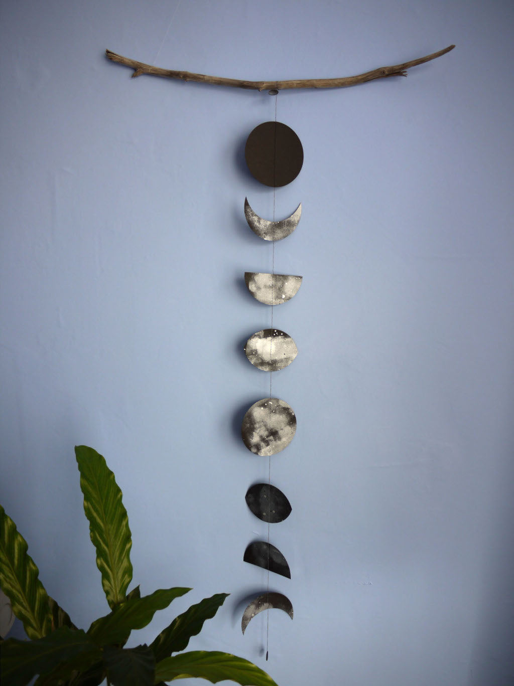 Decorative wall hanging with moon phases on a branch against a light blue wall.