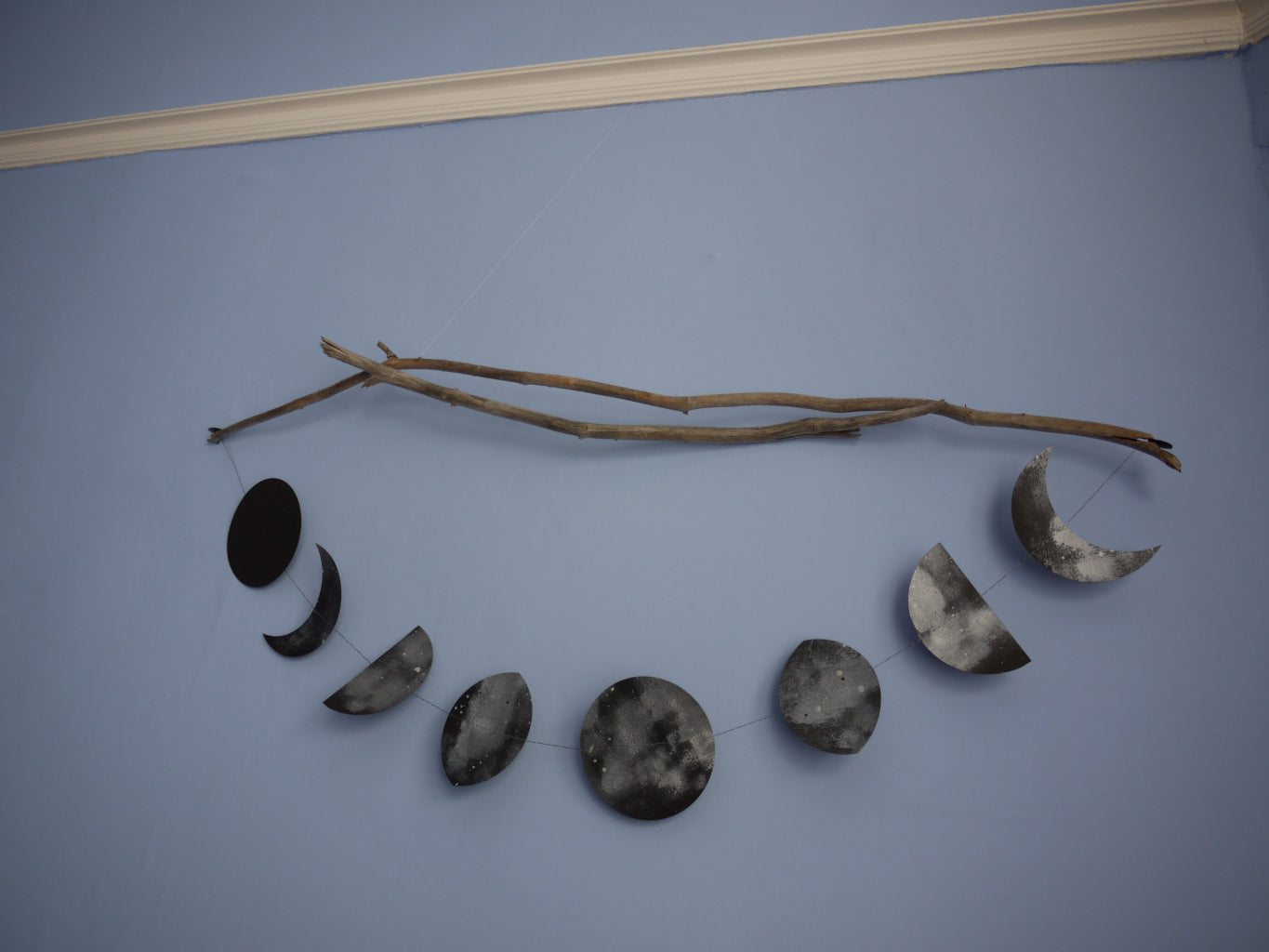 Decorative wall art hung from a branche. Dark and painted moon phases shapes stitched to make a garland from paper 