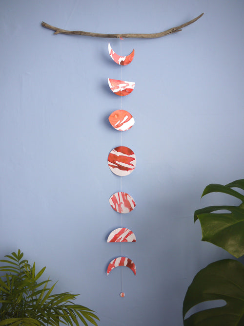 Red and white moon phases shapes paper garland on a blue background, plant in foreground