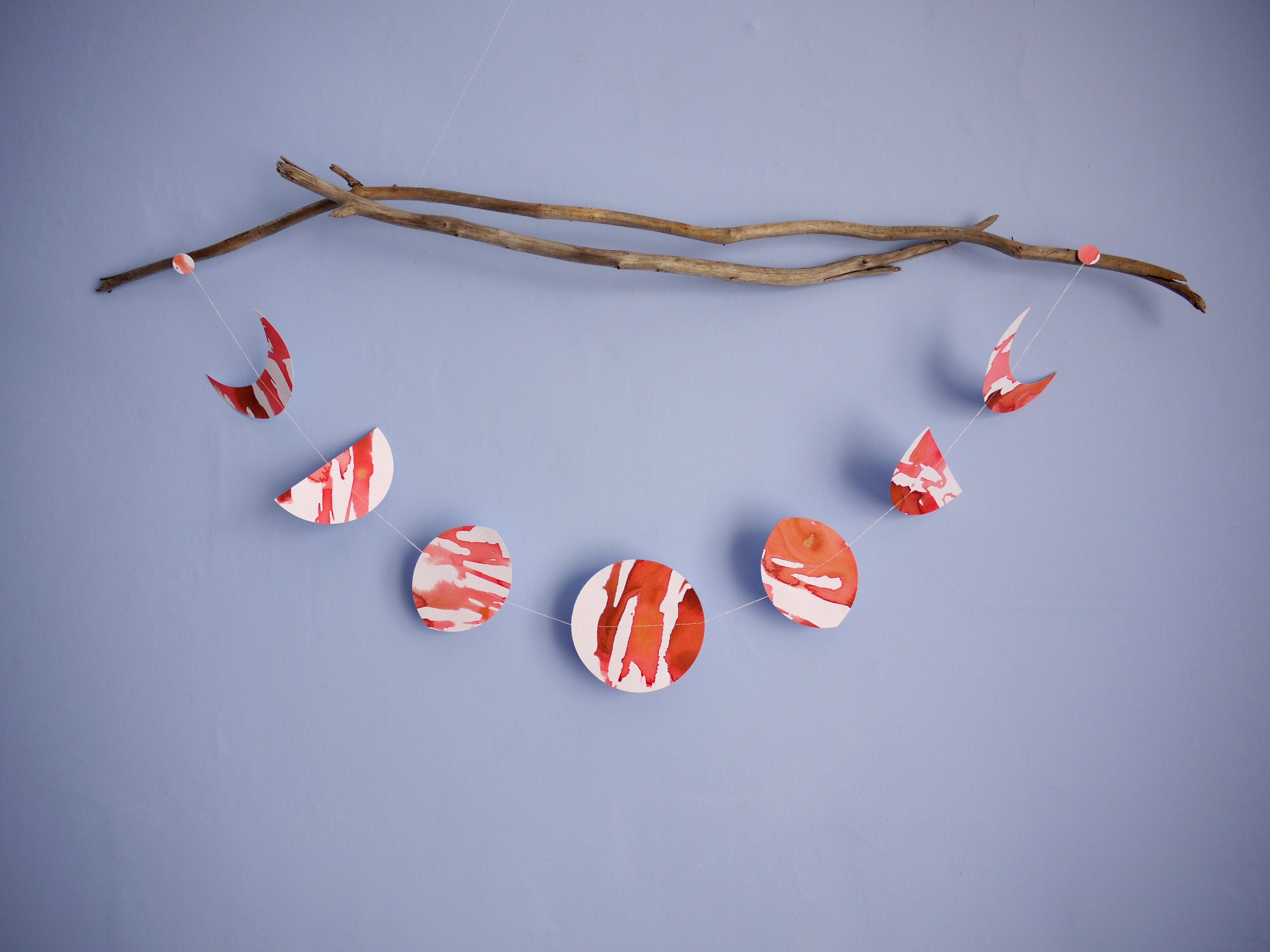 Red and white moon phases garland hung horizontally from driftwood on a blue background
