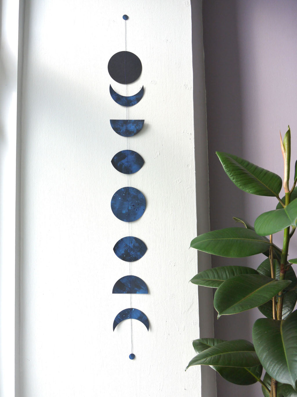 Decorative wall hanging with blue moon phases next to a plant. Handmade paper garland
