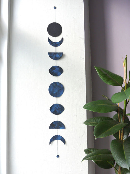 Decorative wall hanging with blue moon phases next to a plant. Handmade paper garland
