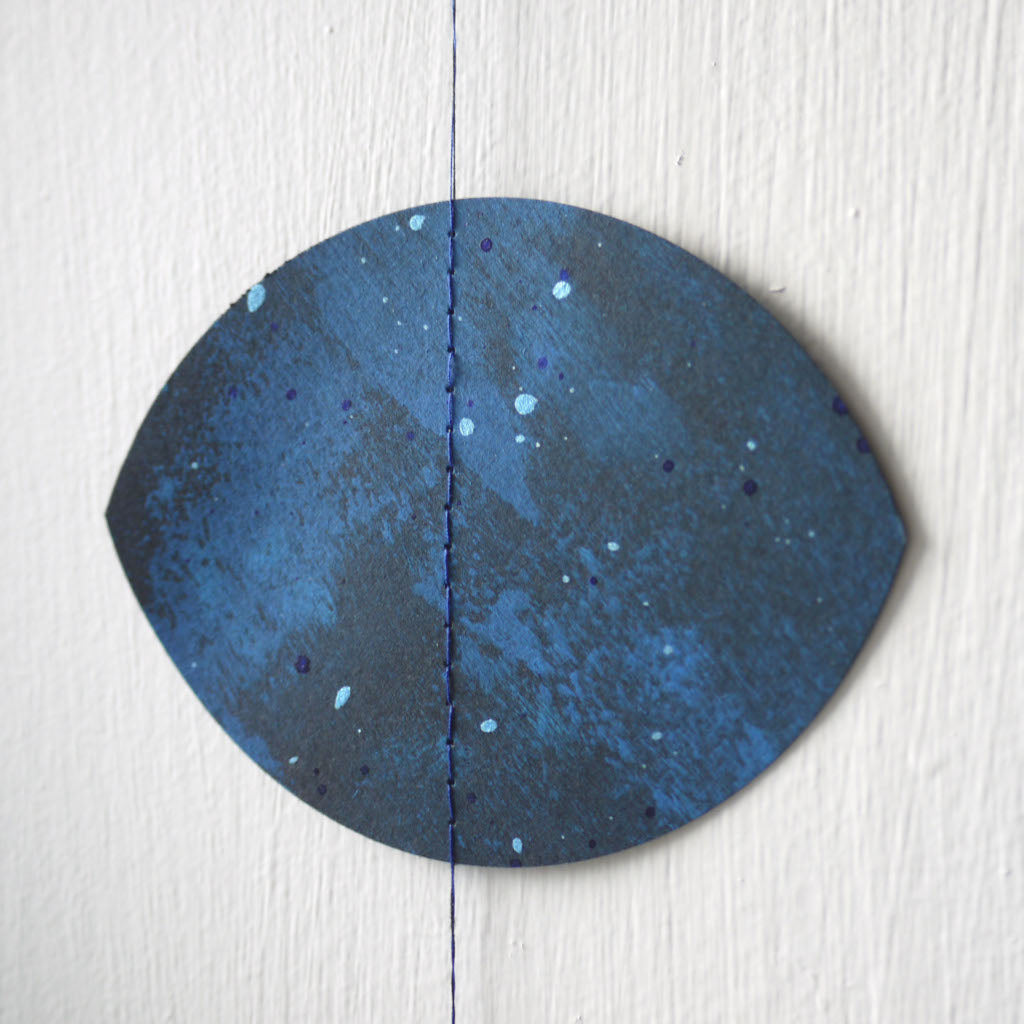 Blue painted details on a black moon phase shape, part of a moon phases wall hanging.