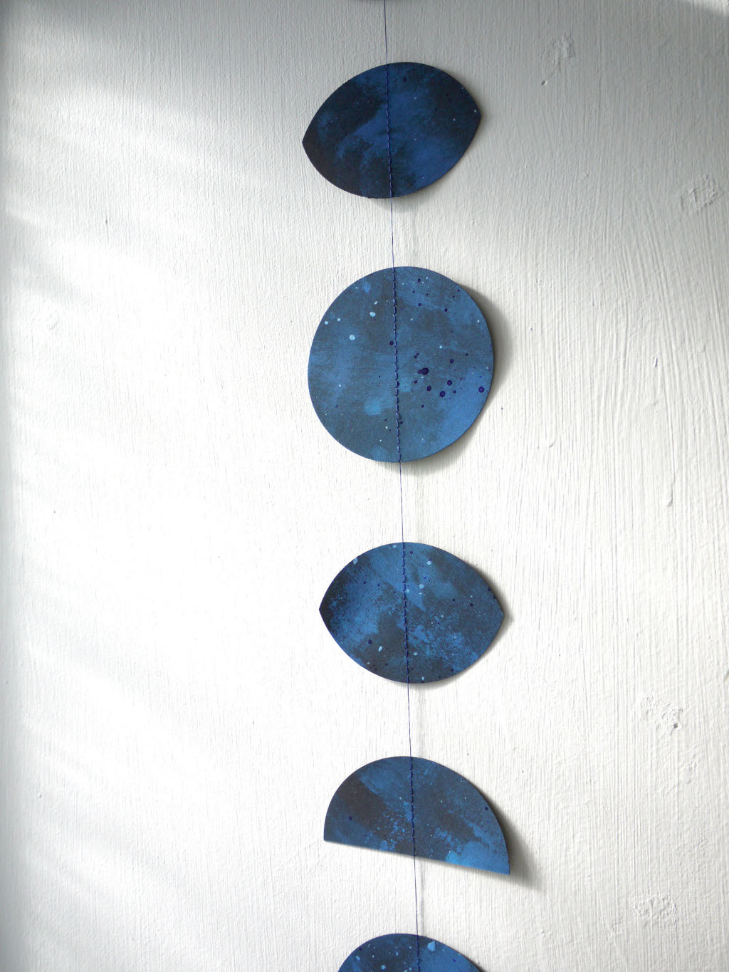 Sewn paper garland of blue moon phases shapes on a white wall