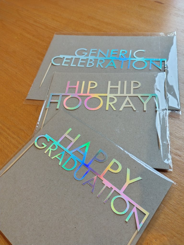 A selection of holographic celebration cake toppers including graduation theme cake, made in Scotland