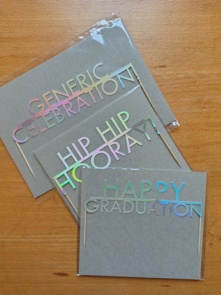 A selection of holographic celebration cake toppers made in Scotland. Includes graduation theme cake topper.
