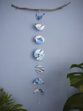 Paper garland of phases of the moon painted with blue and black ink stitched to create a wall hanging displayed on a blue background with plants either side