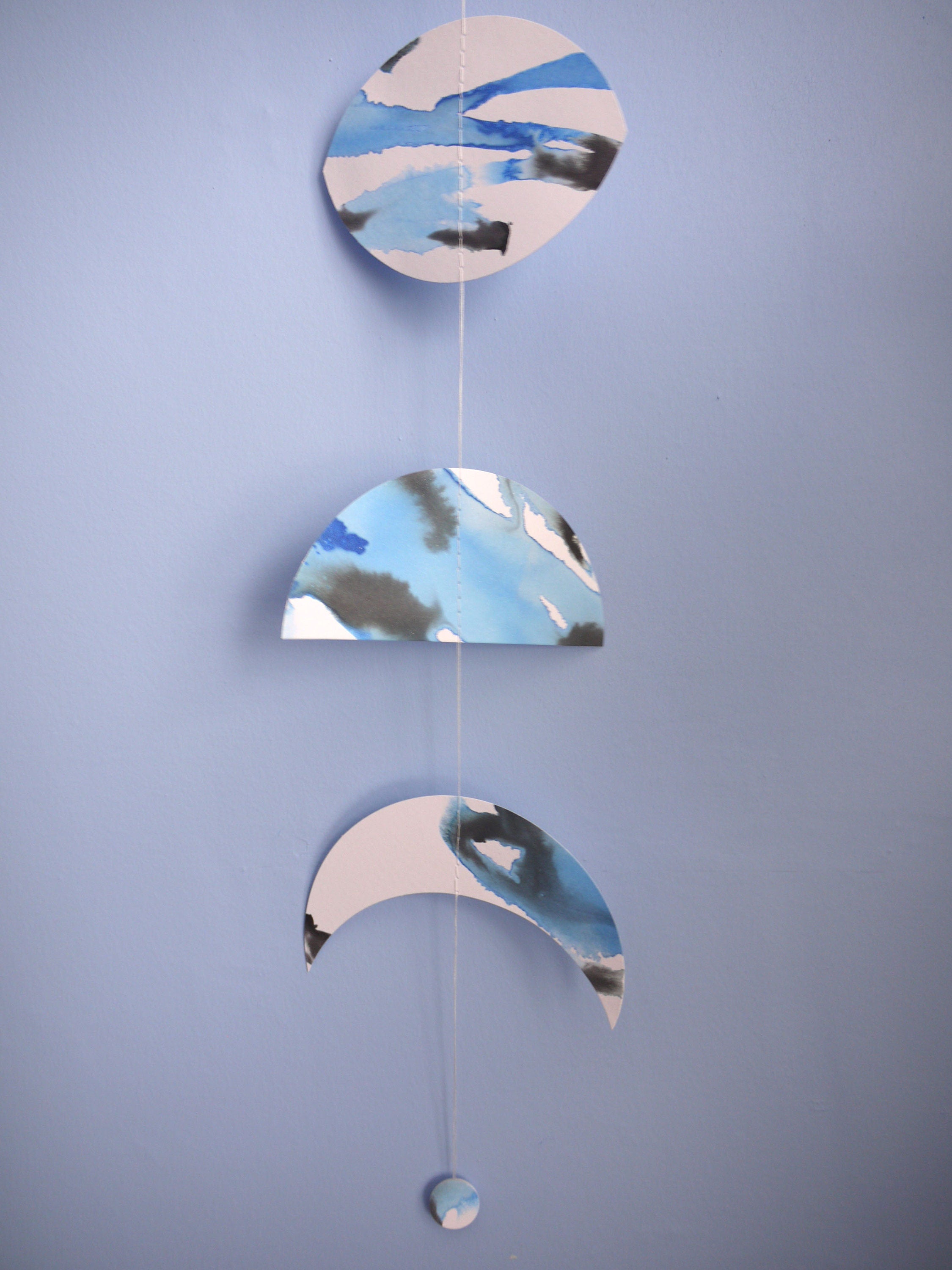 Close up of moon phase wall garland painted with blue and black ink hanging on blue wall