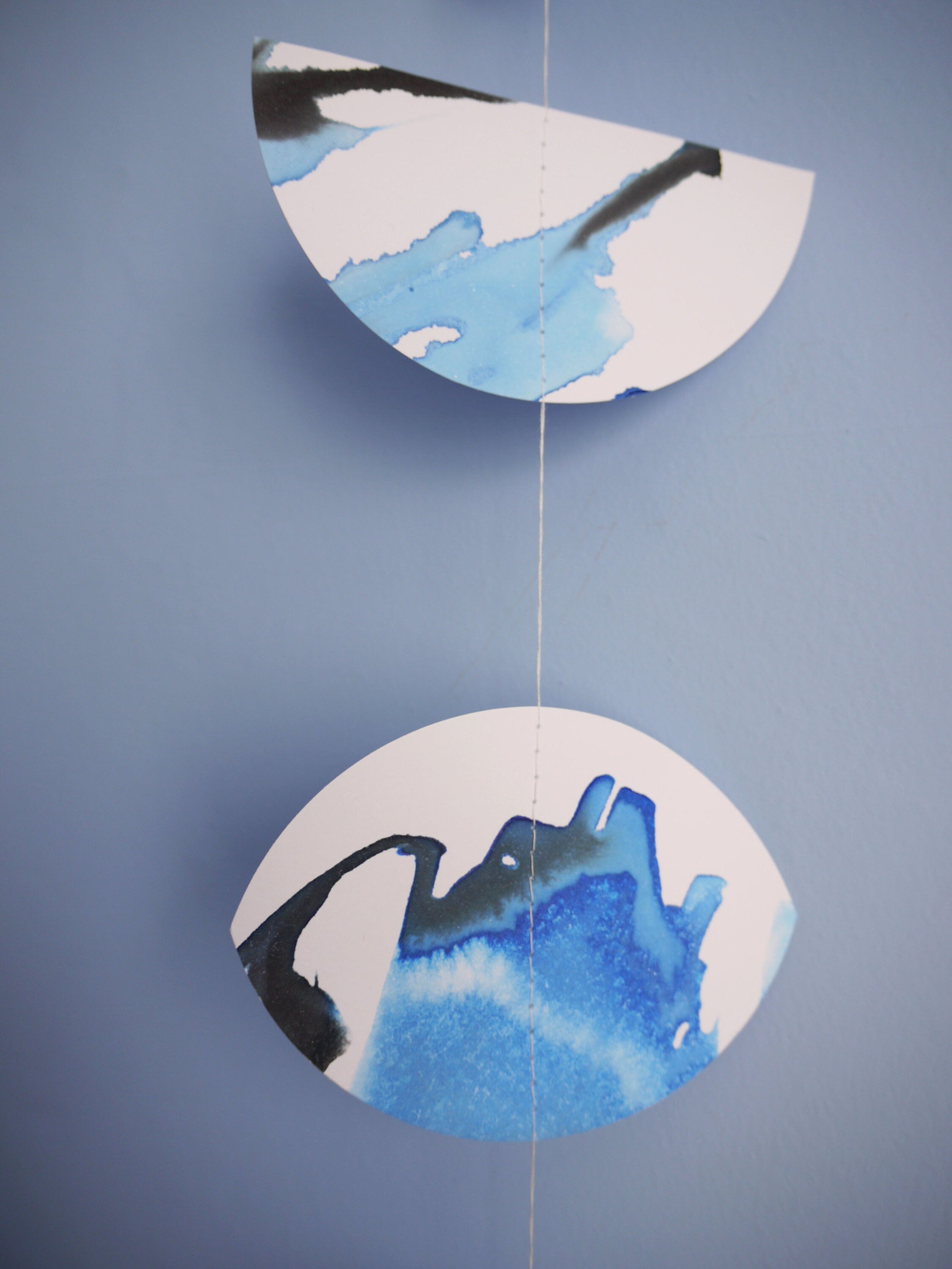 Blue and black ink on stitched paper garland shaped like phases of the moon on a blue background 