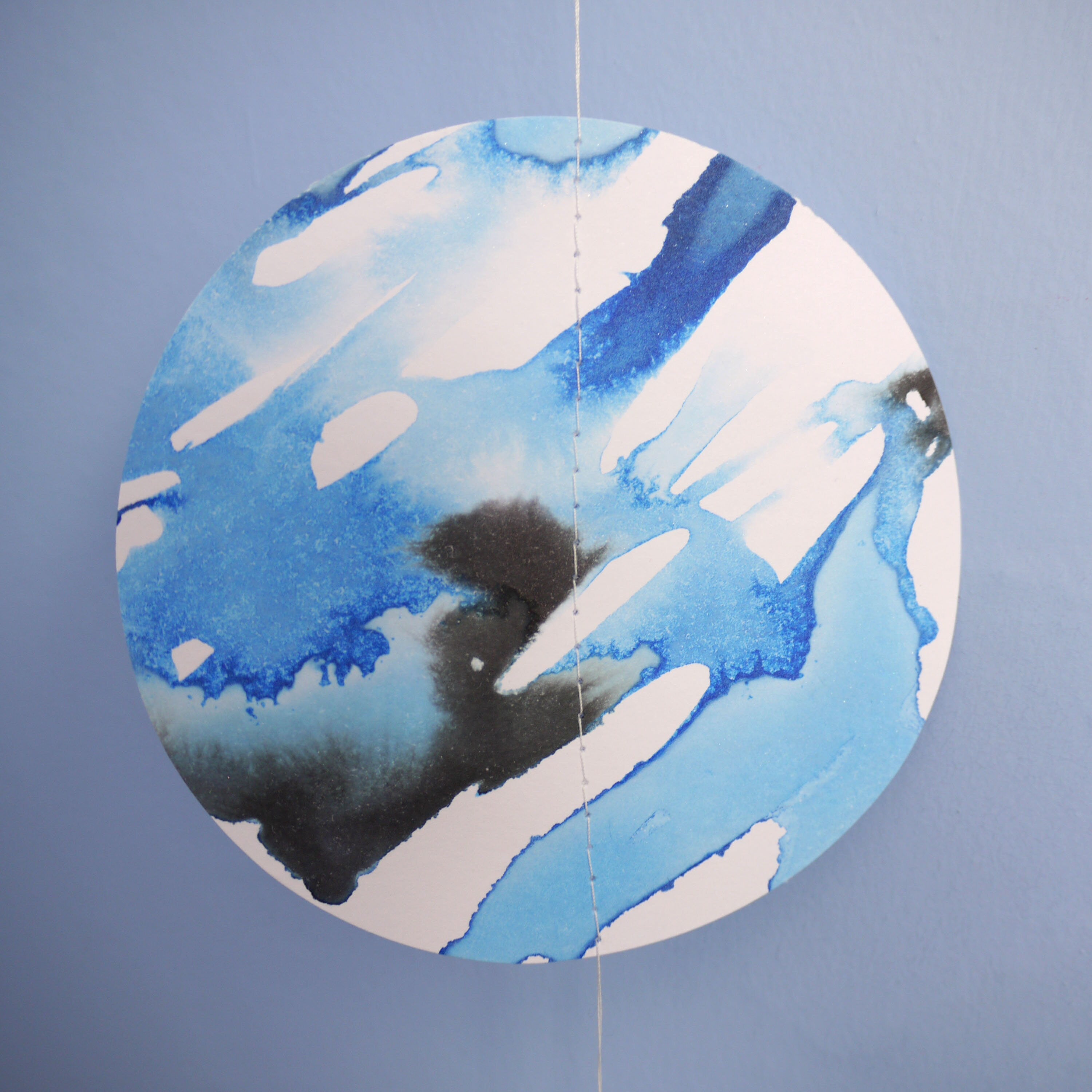 Close up of cold moon garland full moon shape painted with blue and black ink stitched to create a wall hanging displayed on a blue background 