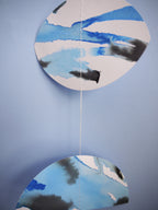 Moon phase shapes painted with blue and black ink stitched to create a wall hanging displayed on a blue background 