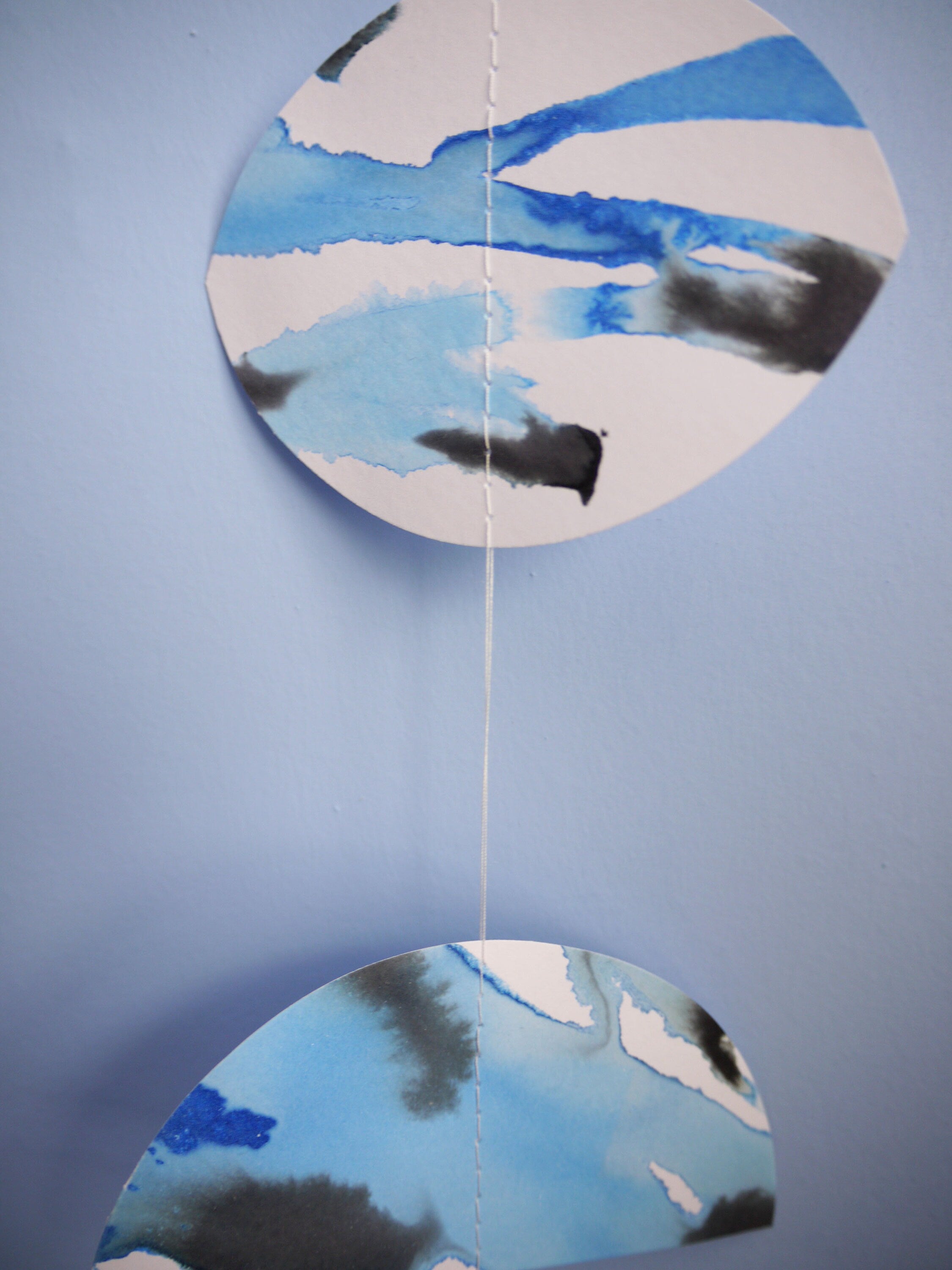 Moon phase shapes painted with blue and black ink stitched to create a wall hanging displayed on a blue background 