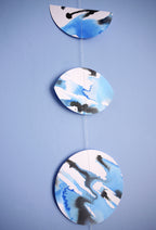 Moon phase shapes painted with blue and black ink stitched to create a wall hanging displayed on a blue background 