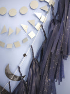 Close up on navy tassels with a silver constellation design beside a black moon phases garland and silver paper decor