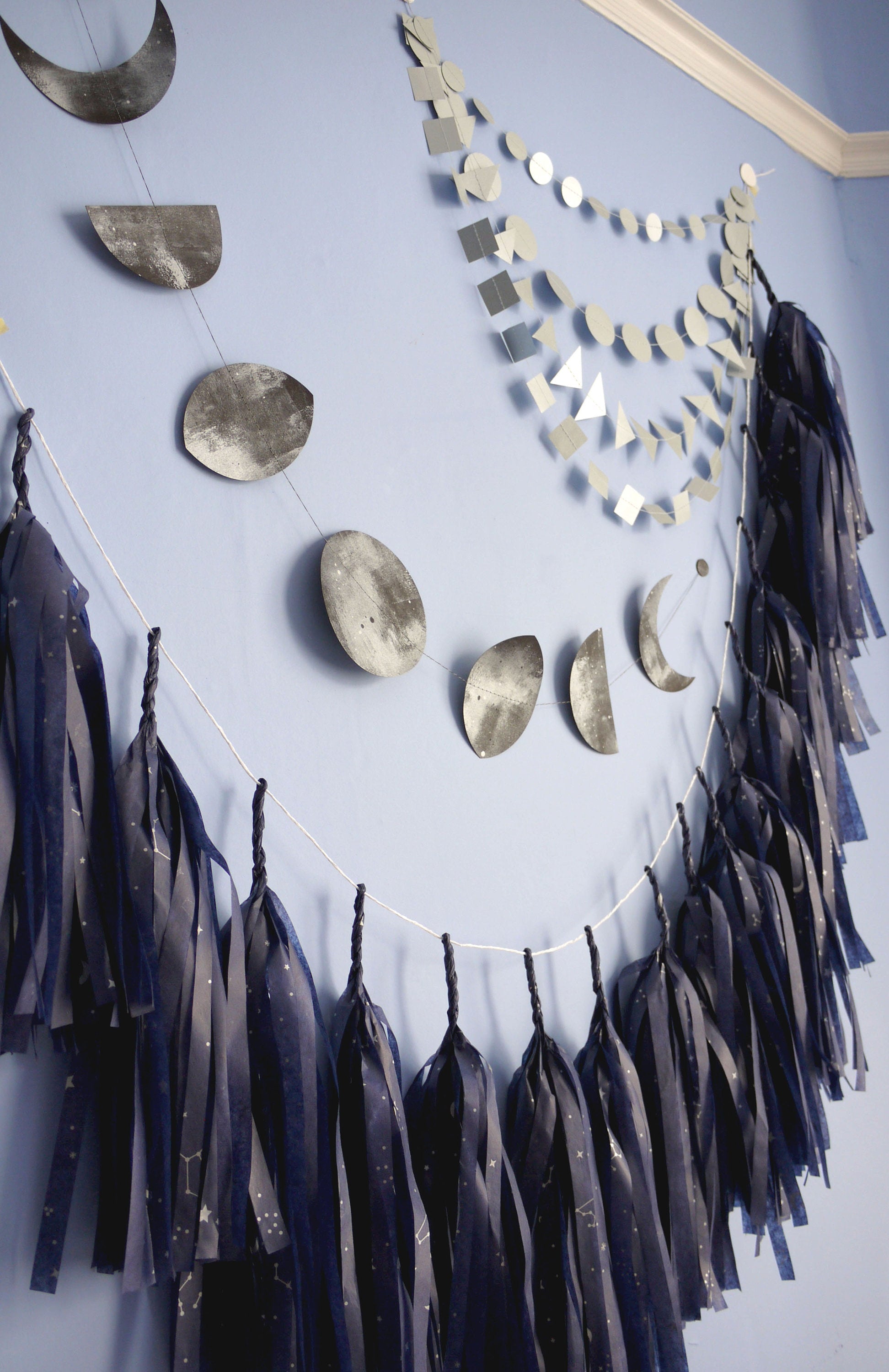 Navy tassel garland with a silver constellation design, a black moon phases garland and silver paper wall hanging