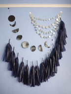 Wall display of navy tassel garland, a moon phases garland and silver paper decor.