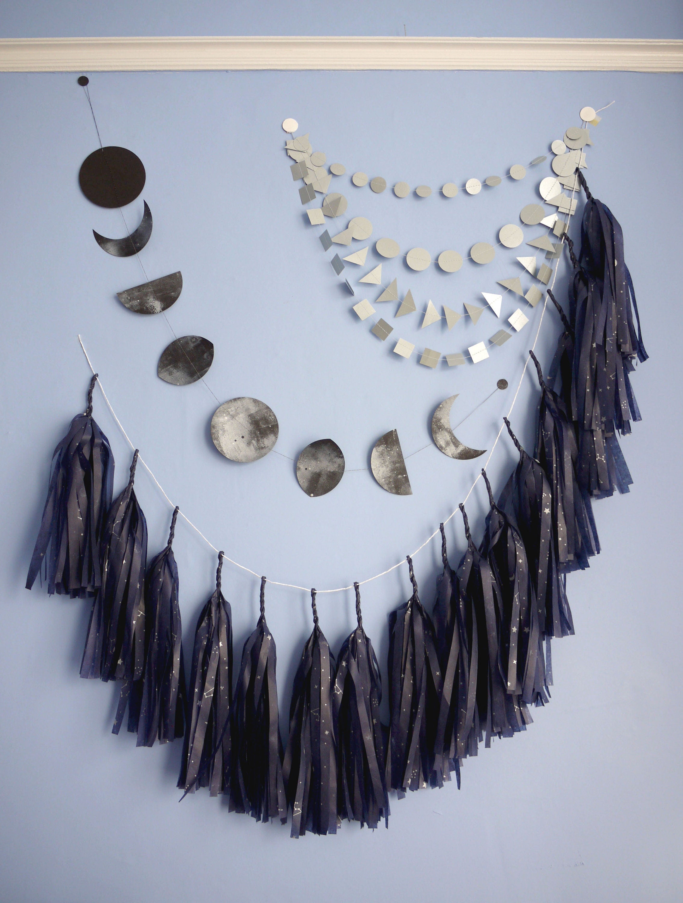 Wall display of navy tassel garland, a moon phases garland and silver paper decor.