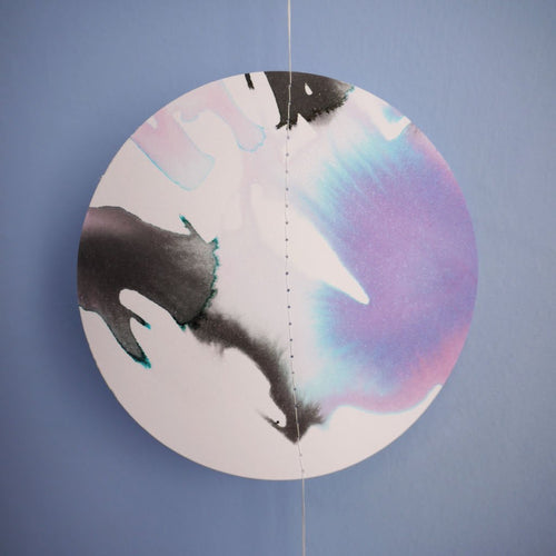 Close up of a full  moon shape stitched paper garland painted with black blue and purple inks hanging  on a blue wall