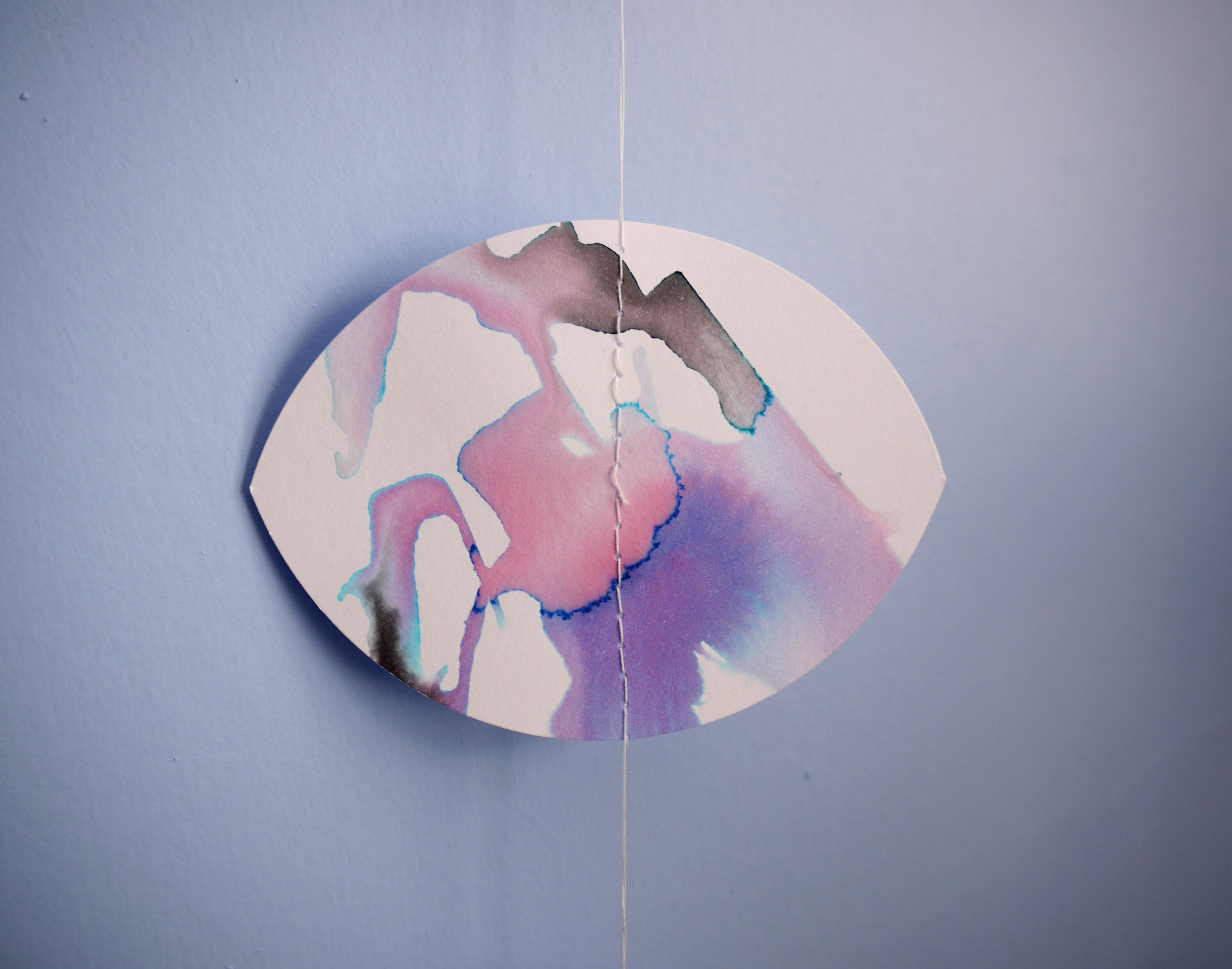 Close up of a moon shape stitched paper garland painted with black blue and purple inks hanging  on a blue wall