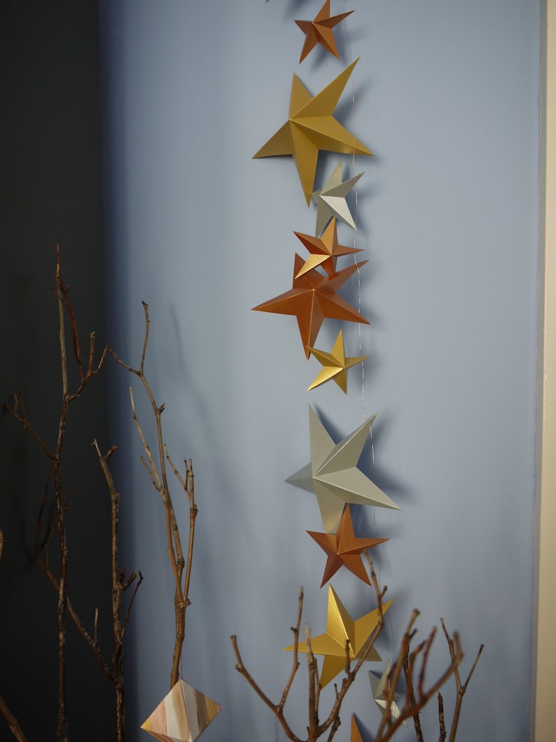 Metallic star garland hands vertically on a blue background with branches 