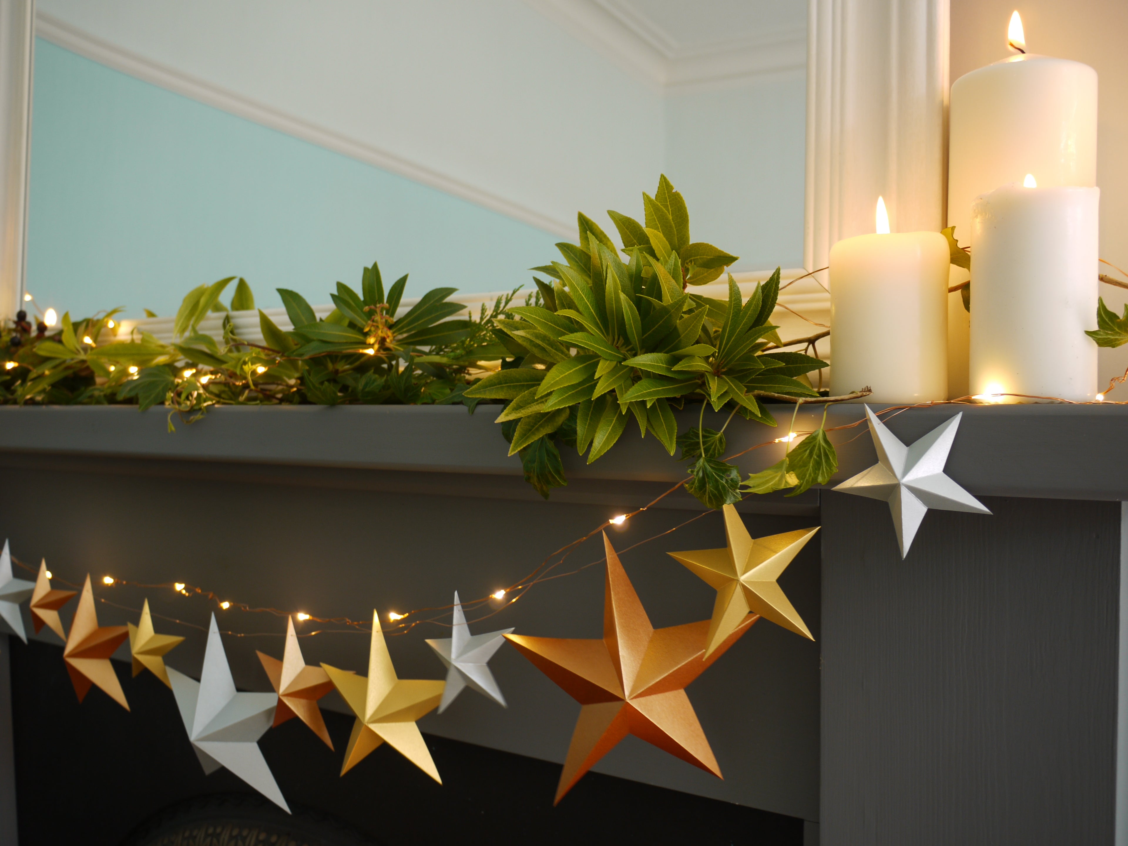Metallic star garland with fairy lights and greenery at fireplace