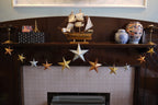Decorative mantel with star garland, vases, and a model ship above a fireplace.