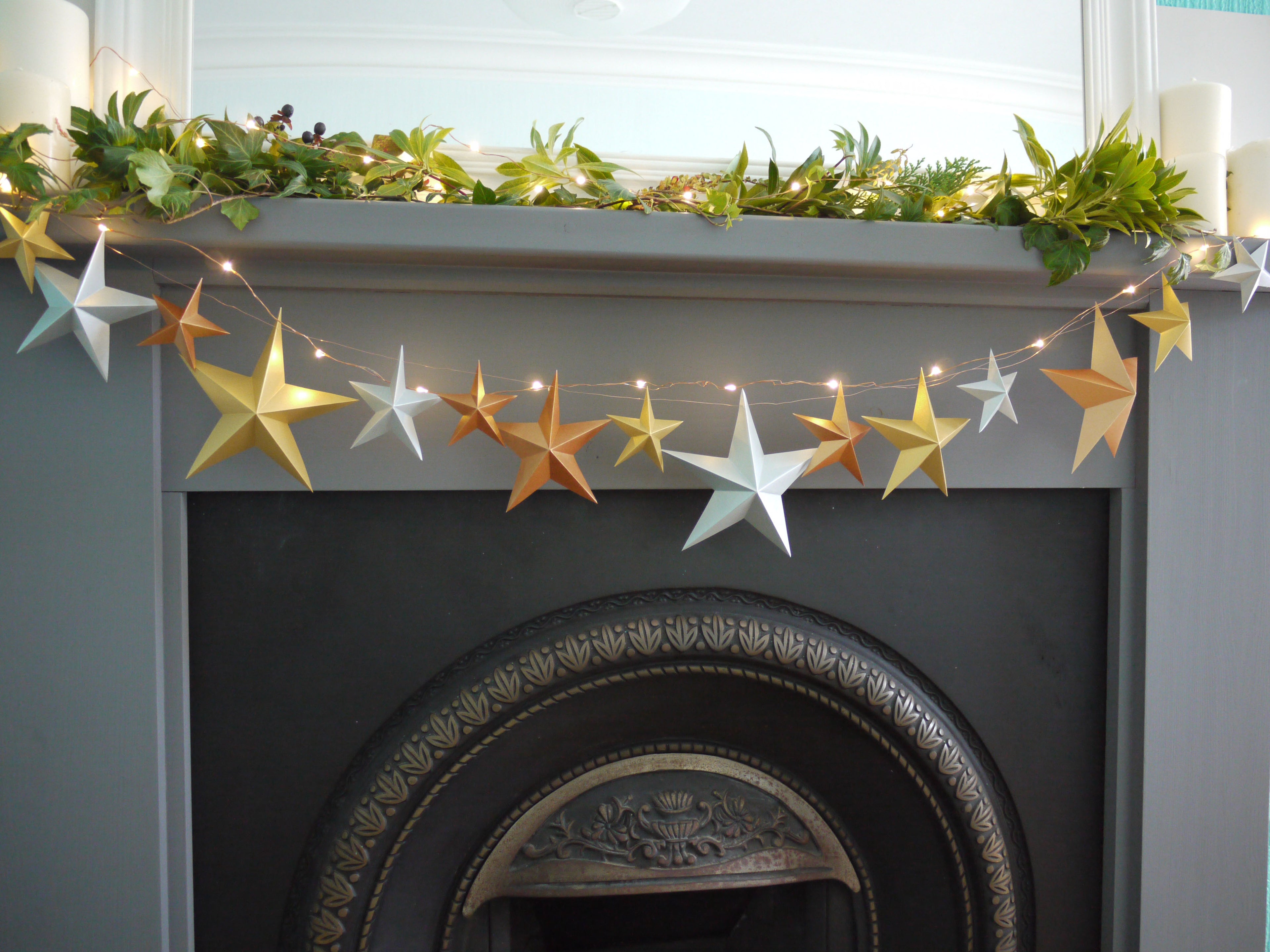 Metallic star garland with fairy lights and greenery at fireplace