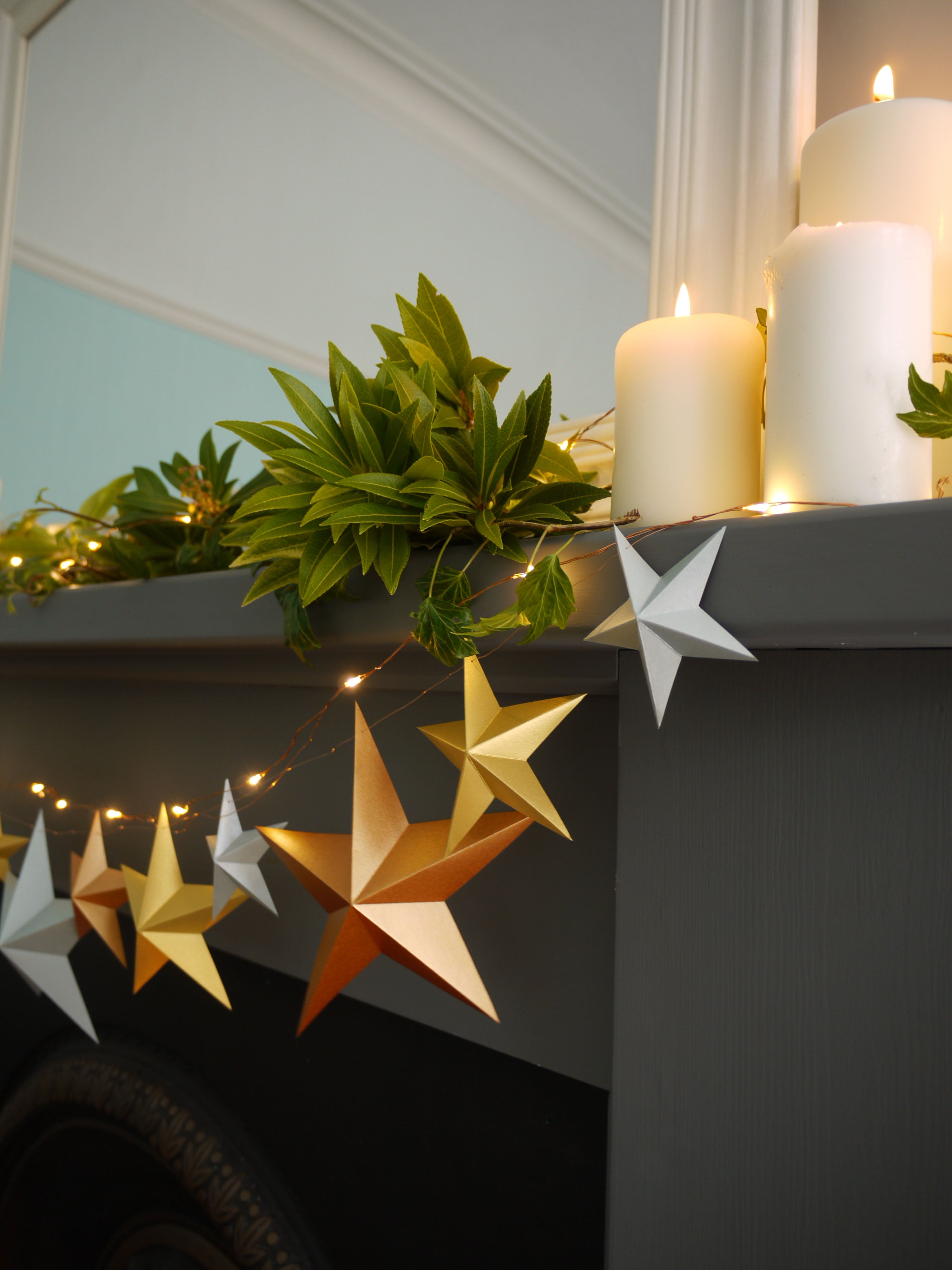 Decorative stars and candles on a mantelpiece with greenery