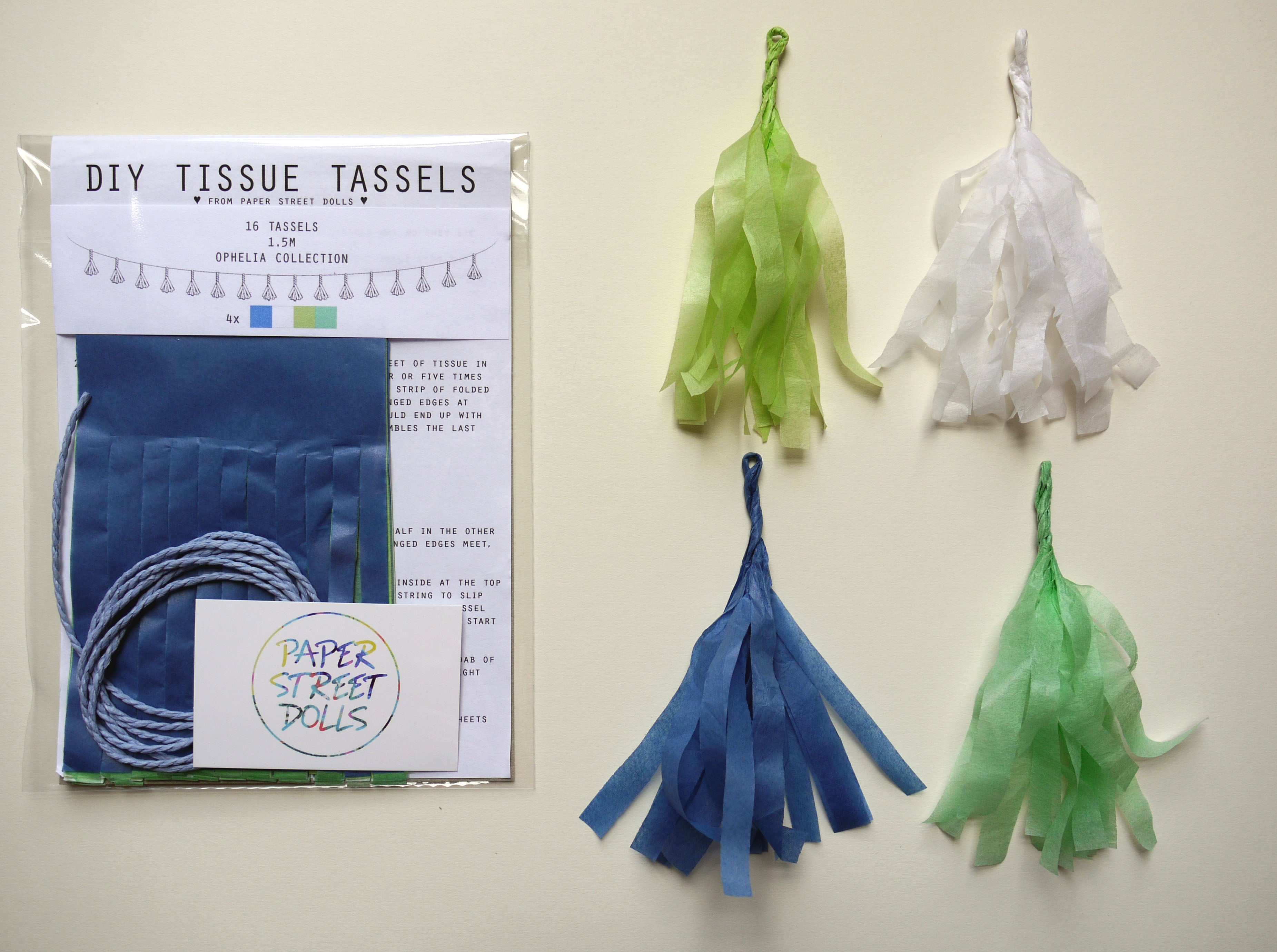 DIY tissue tassels kit with blue yarn, green and white tissue paper, and tassels on a beige background.