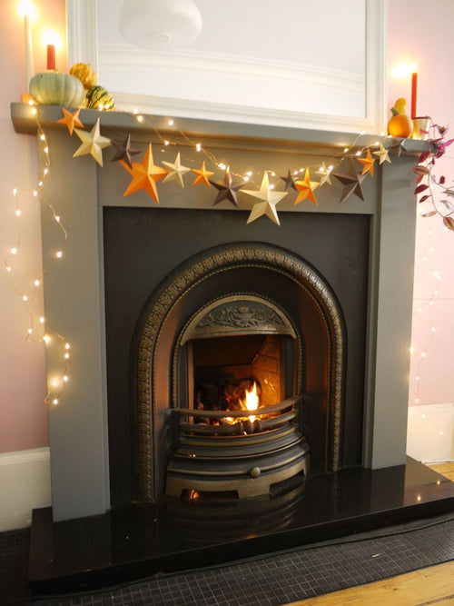 Decorative fireplace with star-shaped garland, lights and pumpkins on a mantel.