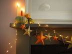 Decorative mantel with star-shaped ornaments and string lights, featuring pumpkins and candles.