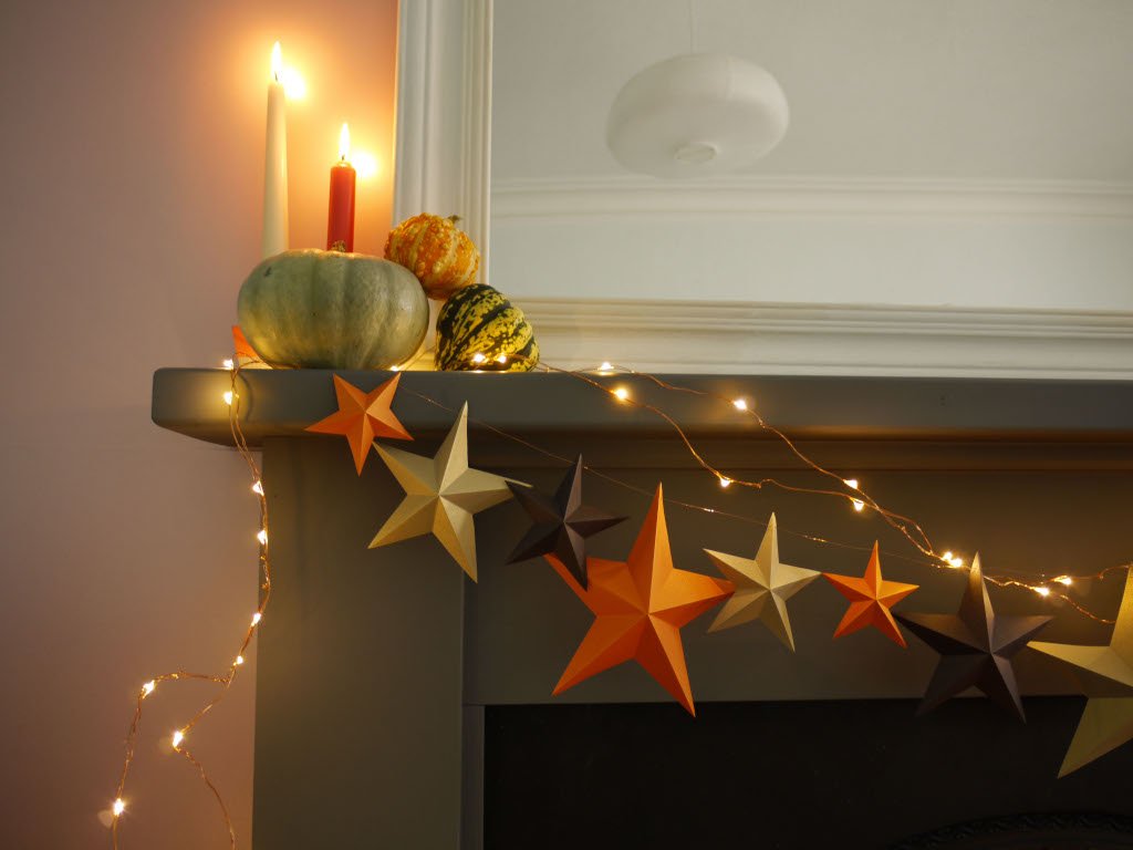 Decorative mantel with star-shaped ornaments and string lights, featuring pumpkins and candles.