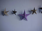 Whimsigoth DIY Samhain decorations. DIY paper star garland of 3D stars in black, purple, and pewter paper hanging against a light blue wall.