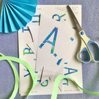 Paper letters with scissors and ribbons on a textured surface