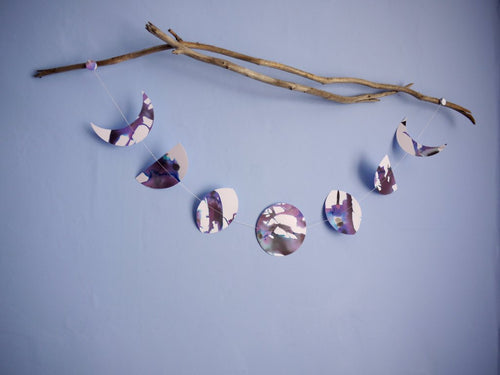 A purple, black and white moon phases wall hanging hanging horizontally from driftwood