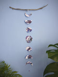 A purple, black and white moon phases wall hanging hanging vertically from driftwood, plants in the foreground