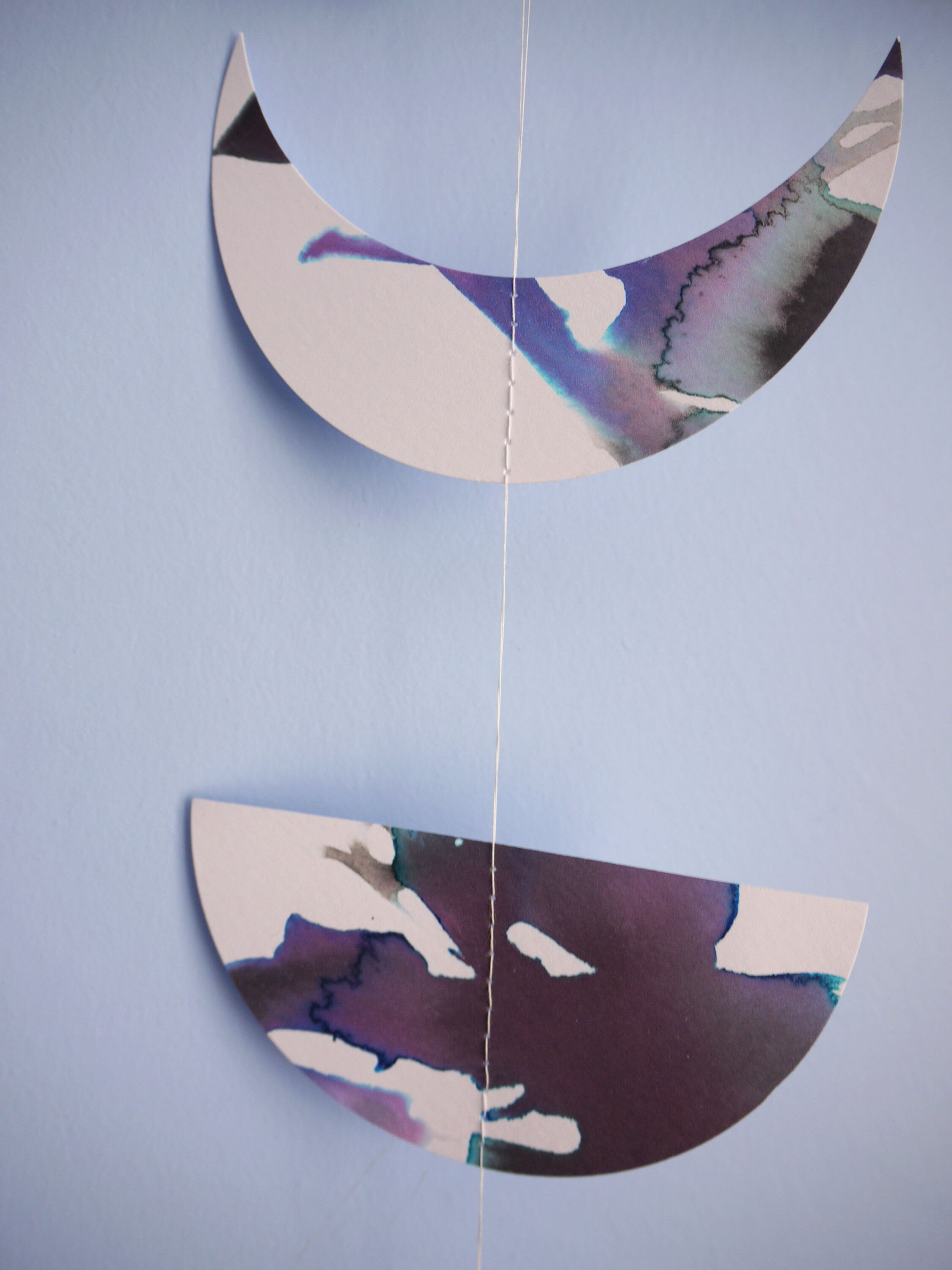 Close up on a crescent and a half moon  shape - purple and black ink painted on white card and stitched to make a moon phases wall hanging.