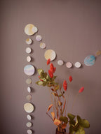 Watercolour painted paper garland in soft pastel tones on a wall, dried flowers in the foreground