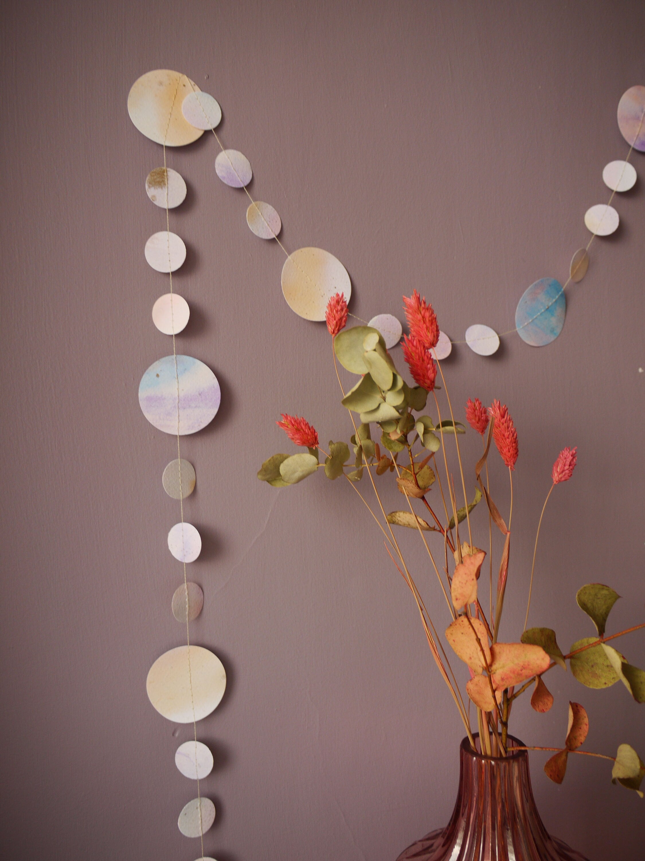 Watercolour painted paper garland in soft pastel tones on a wall, dried flowers in the foreground