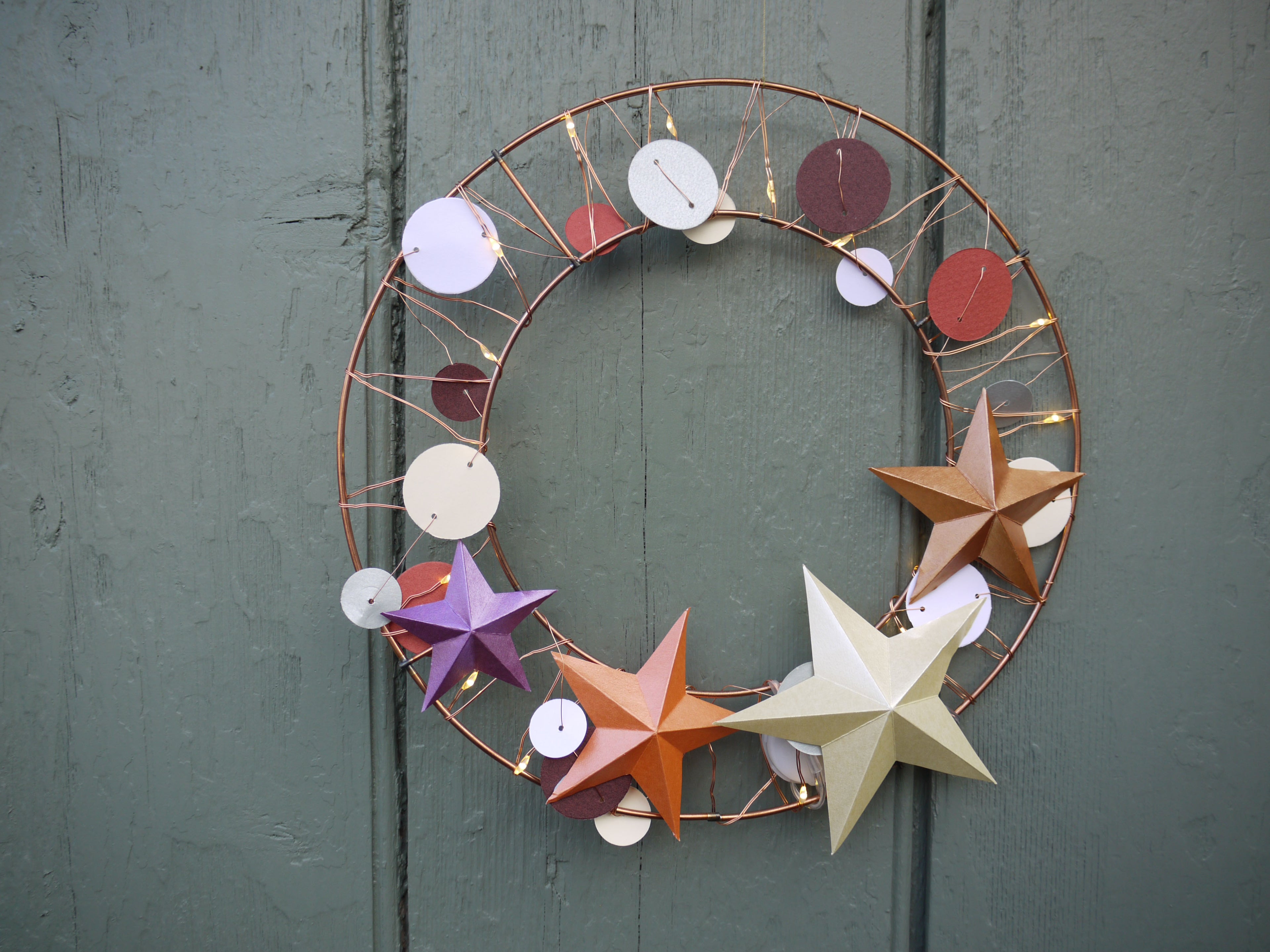Decorative wreath with colorful stars and circular elements on a green wooden door.
