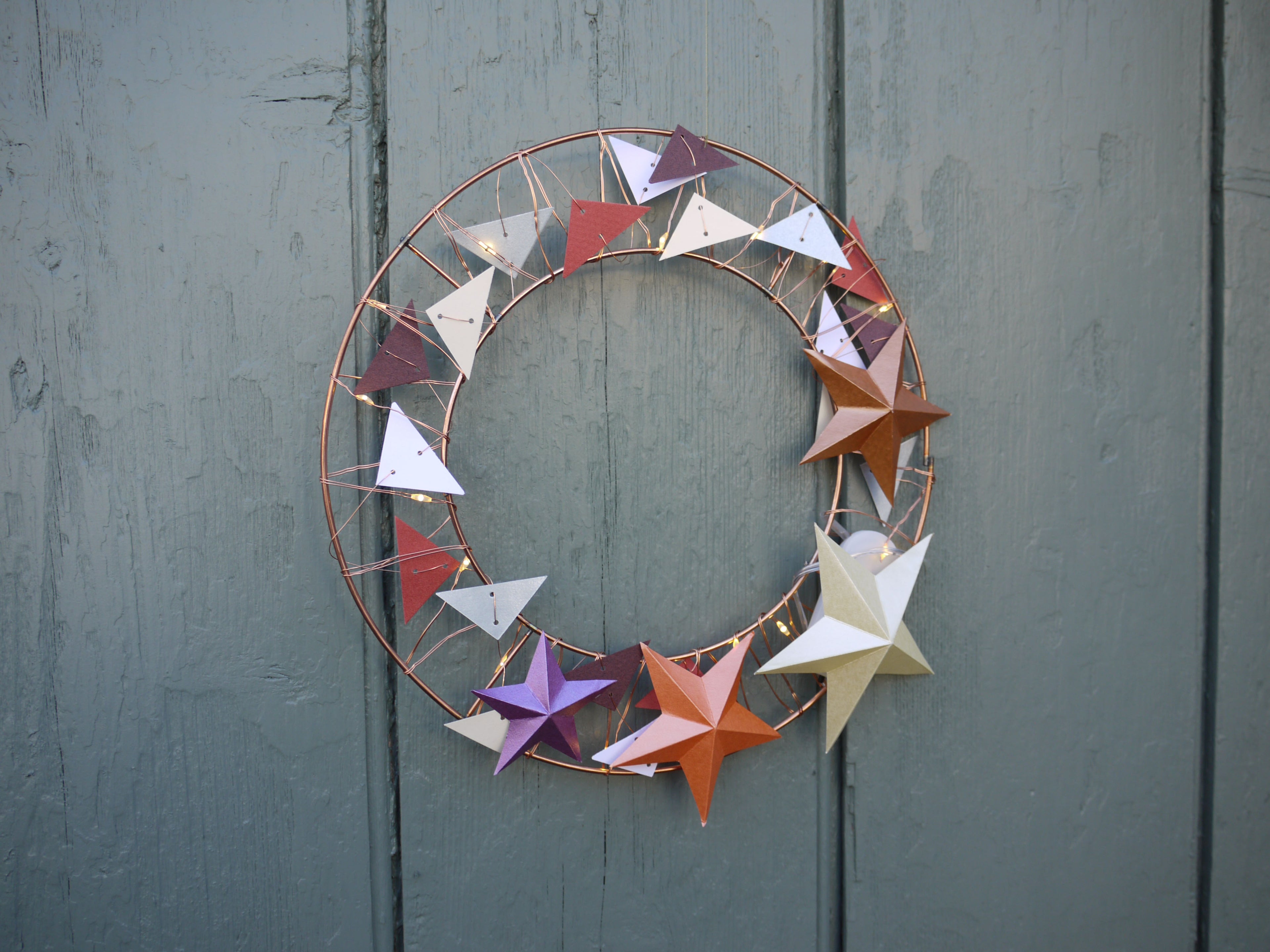 Decorative wreath with colorful star-shaped ornaments on a green wooden door.