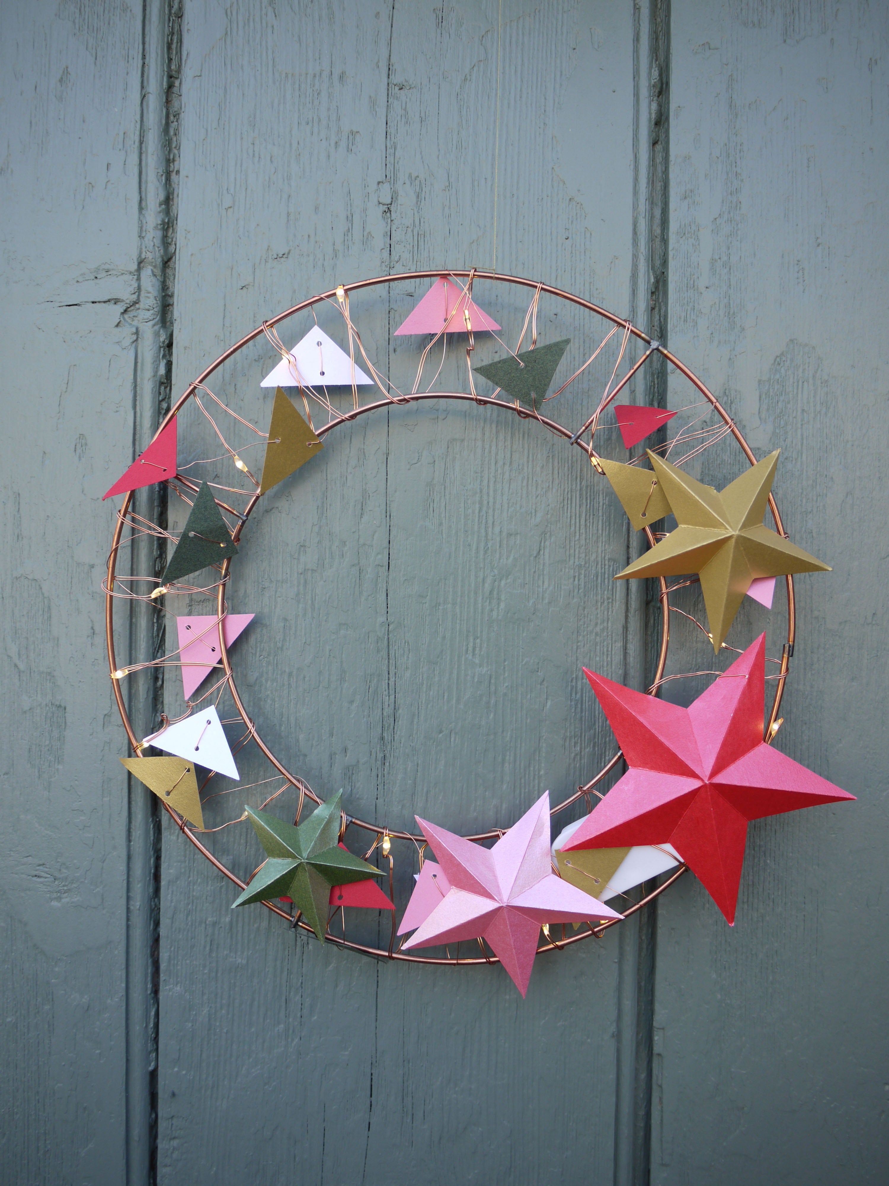 Decorative wreath with colorful paper stars on a wooden door