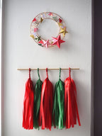 Decorative wreath with colorful stars and tassels hanging on a white wall.