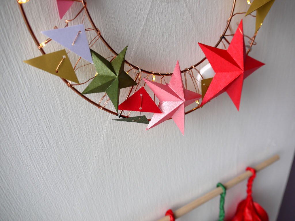 Decorative wreath with colorful paper stars on a plain wall.