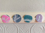 Four circular riso print cyanotype shapes with different botanical and abstract patterns in pink, blue, teal, and purple, stitched together and hung in a hallway.