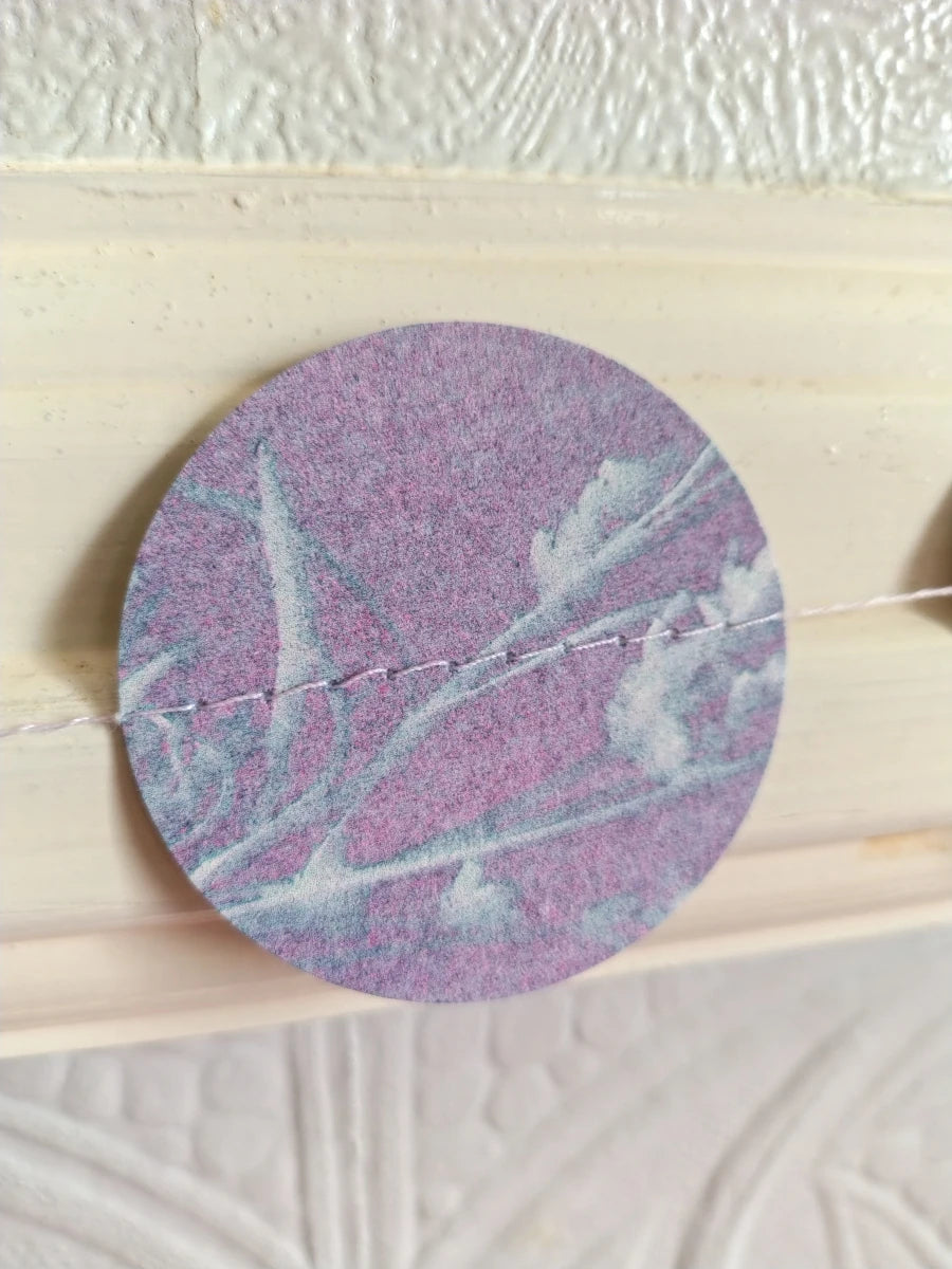 A close-up of a riso print cyanotype circle stitched as part of a paper garland.