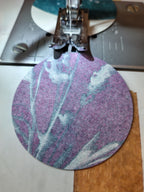 A close-up of a circle with a purple botanical image being fed under a sewing machine presser foot. Everyday Enchantment riso print cyanotype garlands being made.