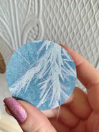 A close-up of a hand holding a circular paper riso shape patch with a light blue  cyanotype design.