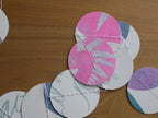 Circular paper garland with pink, white, and blue botanical and abstract patterns, stitched together on a wooden tabletop.